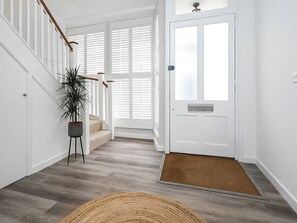 A hallway with a wooden staircase, a potted plant, a white door, and a doormat. - 4 bedroom accommodation in Cromer (Cromer)