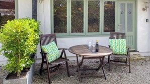 Une terrasse avec deux chaises en bois, une table ronde et un pot de fleurs.