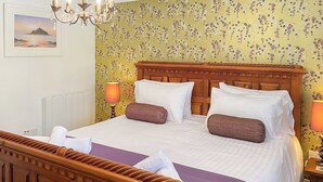 Un lit double avec une tête de lit en bois, deux lampes de chevet et un papier peint à motifs floraux.