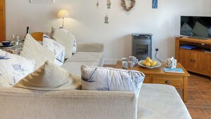 A living room with a sofa set, a table with a lamp, a television, and a fireplace. - Atlantic Cottage - UK48935 (Crowlas, near Penzance)