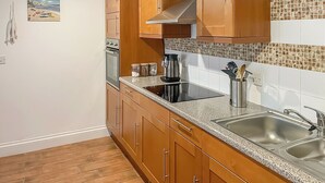 A modern kitchen with wooden cabinets, a stainless steel sink, and a tiled backsplash. - Atlantic Cottage - UK48935 (Crowlas, near Penzance)