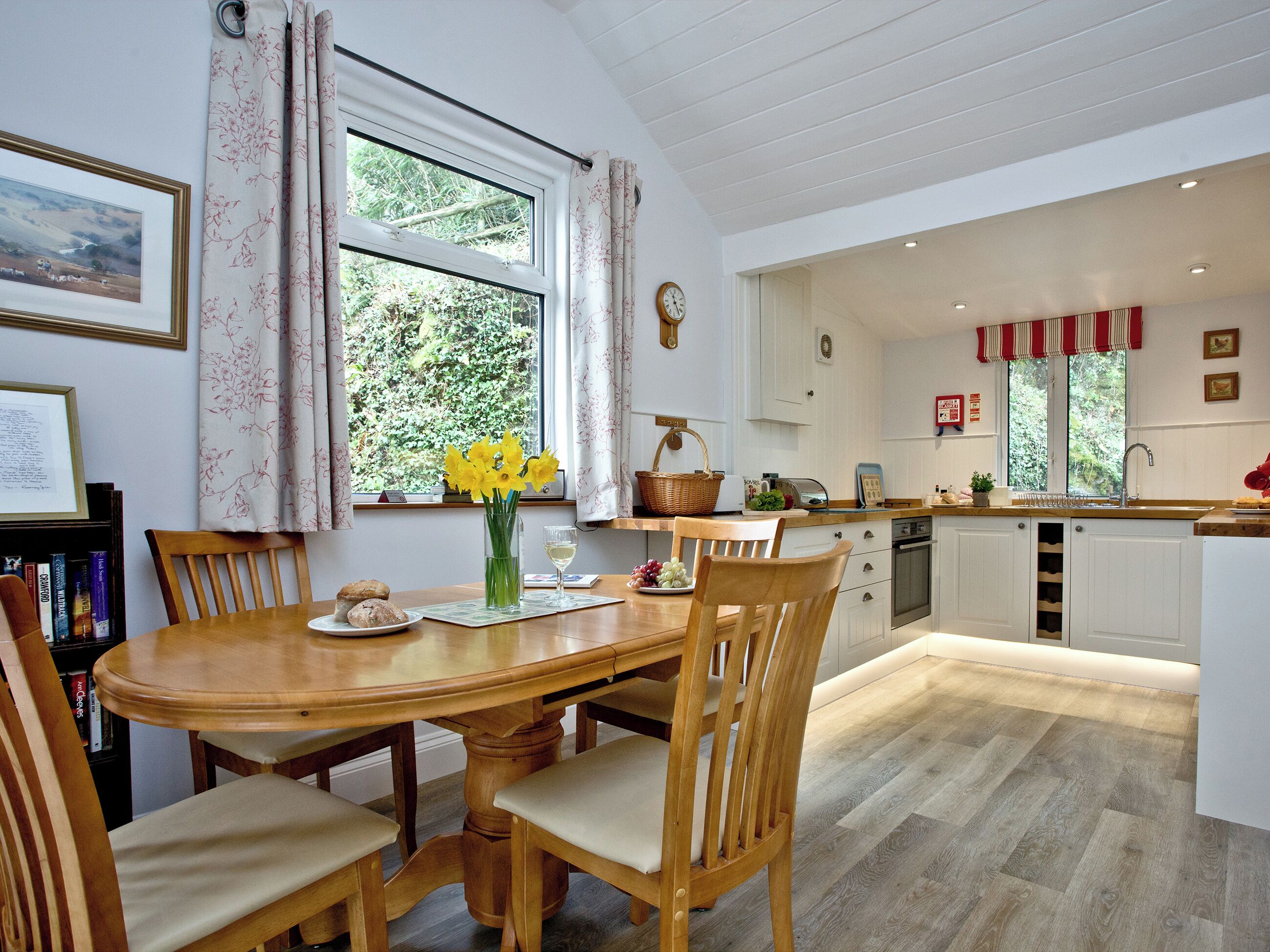 A dining area with a wooden table and chairs, a vase with flowers, and a window with curtains.