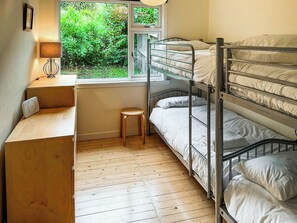 Ein Schlafraum mit Etagenbetten, einem Schreibtisch und einem Hocker, ein Fenster mit Blick ins Grüne sowie eine Lampe auf dem Schreibtisch.