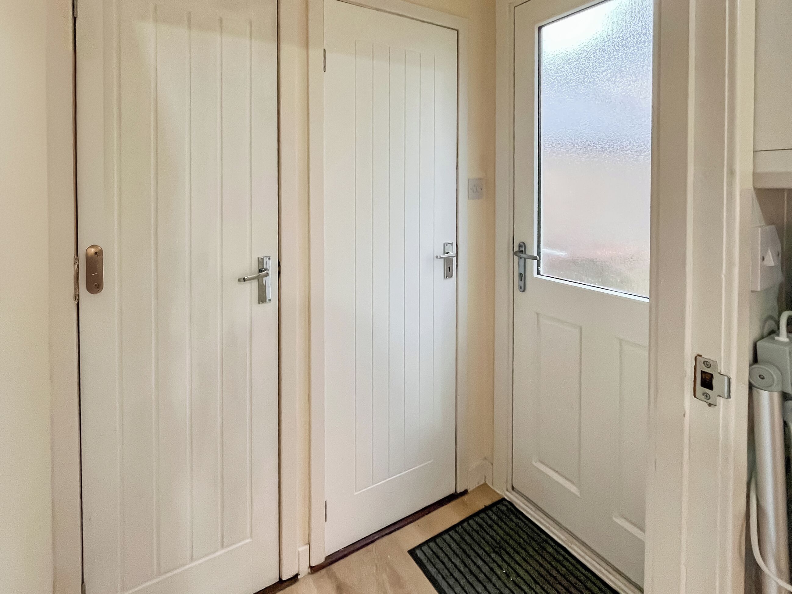 Un conjunto de puertas blancas con un picaporte metálico, una puerta de cristal y un felpudo.