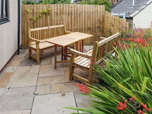 Ein Garten mit Holzmöbeln, einem Tisch und Stühlen, umgeben von einem Holzzaun und verschiedenen Pflanzen.
