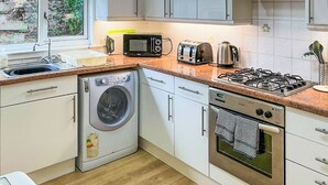 Een compacte keuken met een wasmachine, een magnetron, een broodrooster, een waterkoker en een gasfornuis.