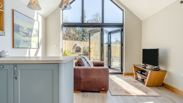 A modern kitchen with a large island, a dining area with a brown sofa, and a TV on a wooden stand. - 1 bedroom accommodation in Mold and the Clwydian Range (Mold and the Clwydian Range)