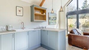 A modern kitchen with light blue cabinets, a white countertop, and a built-in wooden shelf above the sink. There is a framed picture on the wall and a window providing natural light. - 1 bedroom accommodation in Mold and the Clwydian Range (Mold and the Clwydian Range)