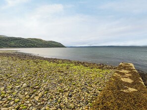 Ein kiesiger Strand mit einer Steinmauer und ruhigem Wasser.