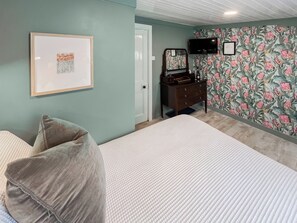 A bedroom with a bed, a dresser, a mirror, a framed picture on the wall, and a television mounted on the wall. - Back Row Bothy - UK37313 (Lochranza)