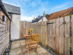 A wooden deck with a table and chairs, a wooden fence, and a house in the background. - Apostles Back House - UK37313 (Lochranza)