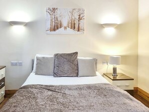 Un dormitorio ordenado con cama, almohadas, una lámpara de noche e imagen colgada en la pared.