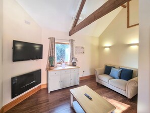 Una sala de estar con televisor, sofá, mesa de centro y una ventana con cortinas.