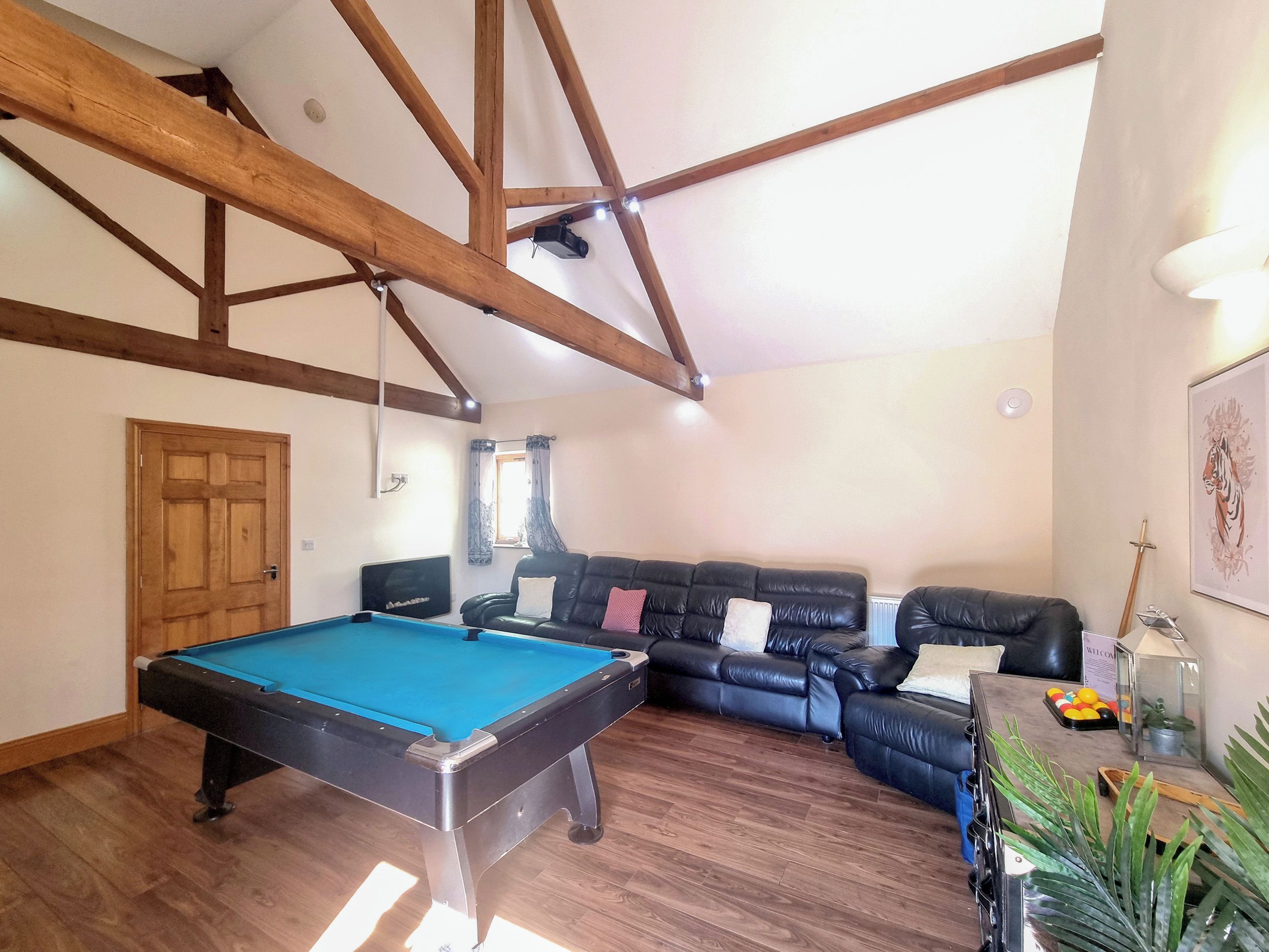 Ein Zimmer mit Pooltisch, Ledersofa, Holzbalken an der Decke und einer Tür.