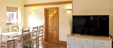 Un comedor con una mesa y sillas de madera, un televisor sobre un mueble, y una puerta que da a otra habitación.
