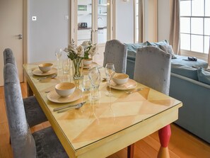 Ruokapöytä on katettu valkoisilla kulhoilla, laseilla ja valkoisten kukkien maljakolla.