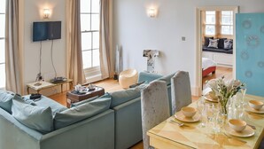 En moderne stue med en sofa, et spisebord dækket til to personer, og et fjernsyn ophængt på væggen.