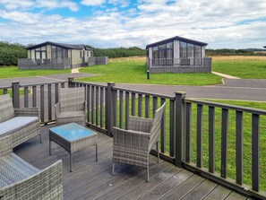 A deck with wicker furniture and a glass table, overlooking a grassy area with two buildings in the background. - 3 bedroom accommodation in Fitling, near Burton Pidsea (Fitling, near Burton Pidsea)