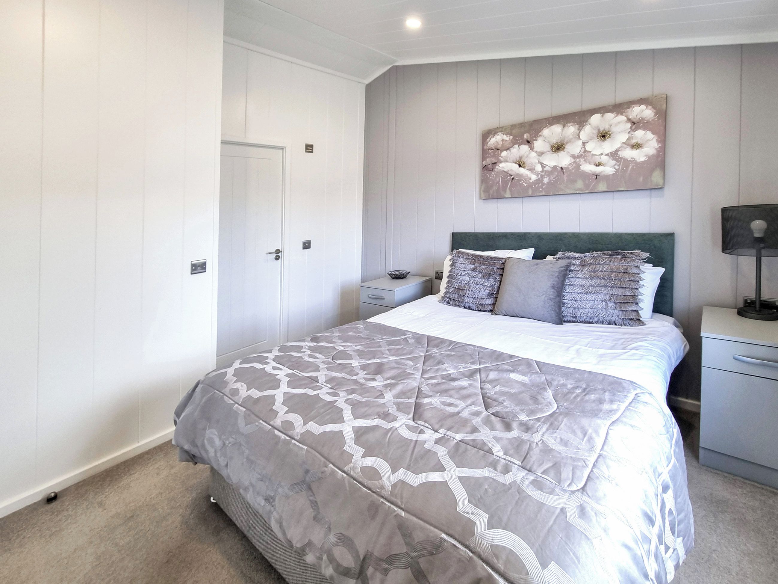 Un dormitorio con cama, mesitas de noche, un cuadro en la pared y una puerta.