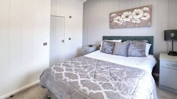 Un dormitorio con cama, mesitas de noche, un cuadro en la pared y una puerta.