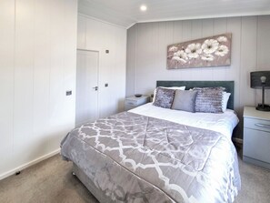 A bedroom with a bed, nightstands, a wall-mounted painting, and a door. - 3 bedroom accommodation in Fitling, near Burton Pidsea (Fitling, near Burton Pidsea)