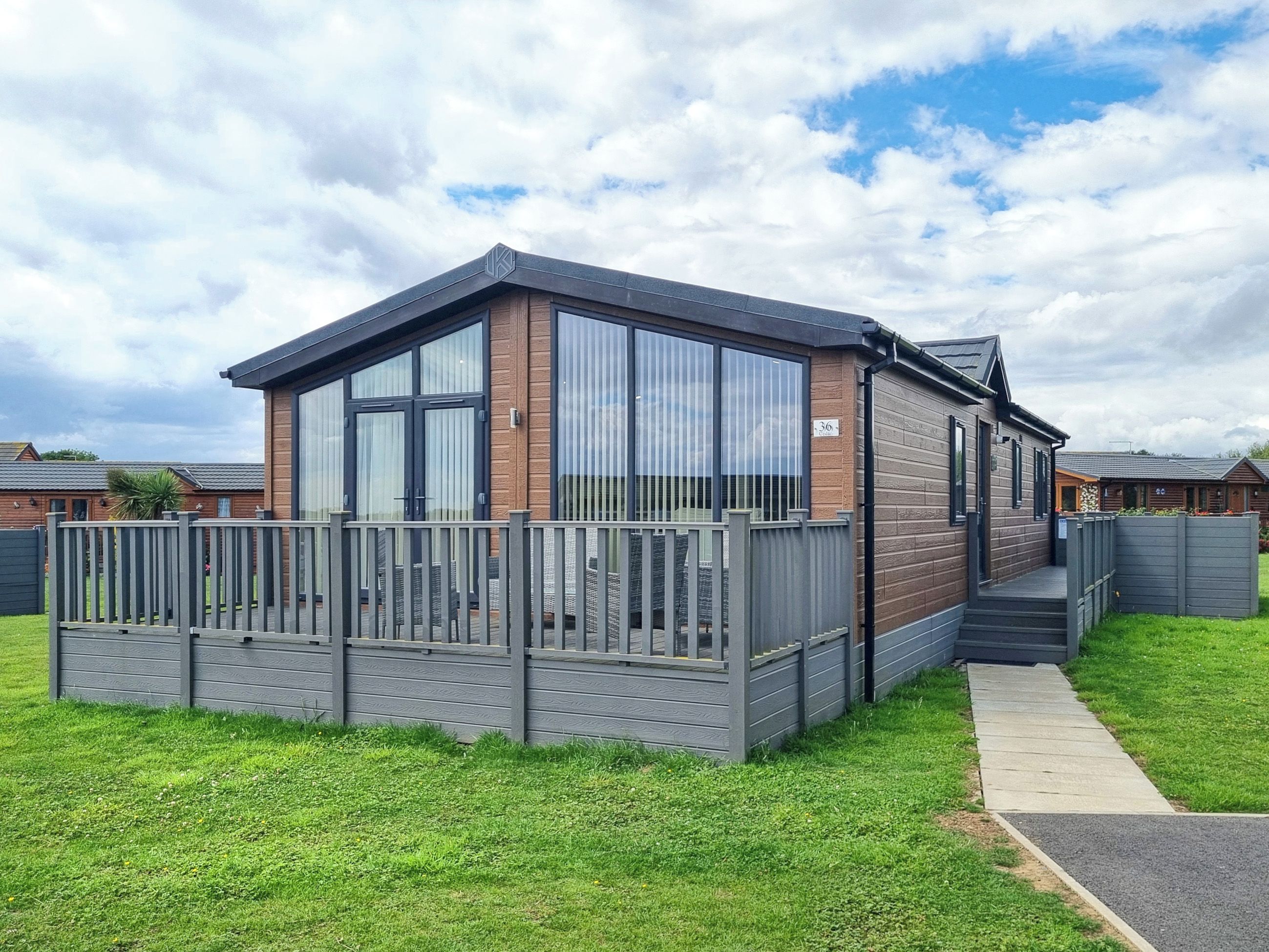 A modern mobile home with a wooden exterior, large windows, and a fenced deck.