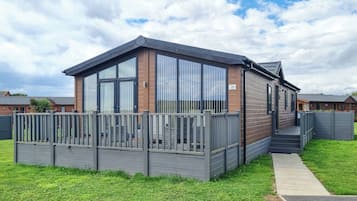 A modern mobile home with a wooden exterior, large windows, and a fenced deck.