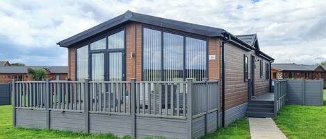 A modern mobile home with a wooden exterior, large windows, and a fenced deck.