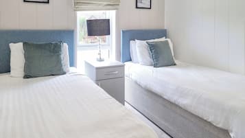A hotel room with two beds, a nightstand, a lamp, and a window with a view of the outside.