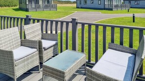 Um terraço com mobiliário de vime e mesa de vidro, com vista para um parque de estacionamento e vários edifícios.