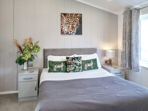Quarto bem arrumado com uma cama grande, duas almofadas com estampas de animais, um quadro na parede de um leopardo, uma mesa de cabeceira com abajur e uma janela com cortinas.