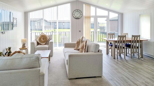 A spacious living room with a high ceiling, a dining area with wooden furniture, and large windows offering a view of the outdoors. - Cherry Blossom 37 - UK50706 (Fitling, near Burton Pidsea)