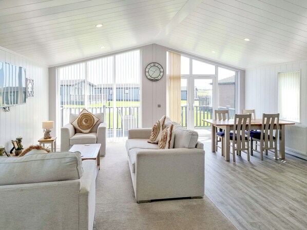 Un vaste salon doté d’un haut plafond, un coin repas avec des meubles en bois et de grandes fenêtres offrant une vue sur l’extérieur.