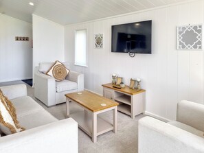 Ett vardagsrum med en soffa, ett soffbord, en TV som är monterad på väggen och dekorativa föremål på ett sidobord.