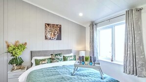 A bedroom with a bed, a nightstand, a window with curtains, a wall-mounted artwork, and a potted plant. - Cherry Blossom 37 - UK50706 (Fitling, near Burton Pidsea)