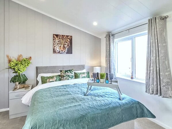 Un dormitorio con cama, mesita de noche, ventana con cortinas, una obra de arte en la pared y una planta en maceta.
