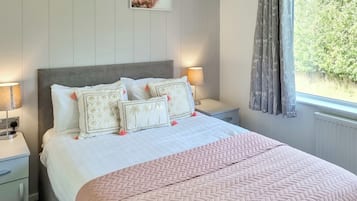 Un letto rifatto con una coperta rosa, due comodini con lampade e due quadri appesi al muro.