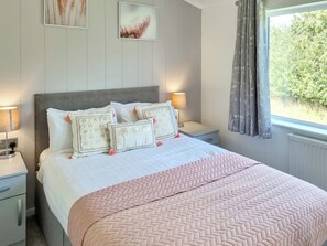 Un lit bien fait, recouvert d’une couverture rose, deux tables de chevet avec des lampes et deux tableaux encadrés accrochés au mur.