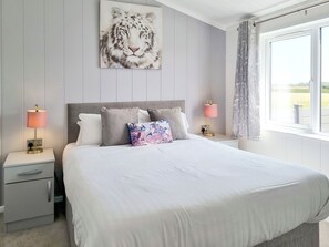 A bedroom with a large bed, two bedside tables with lamps, a nightstand with a drawer, a headboard, and a window with curtains. - Cherry Blossom 38 - UK50707 (Fitling, near Burton Pidsea)