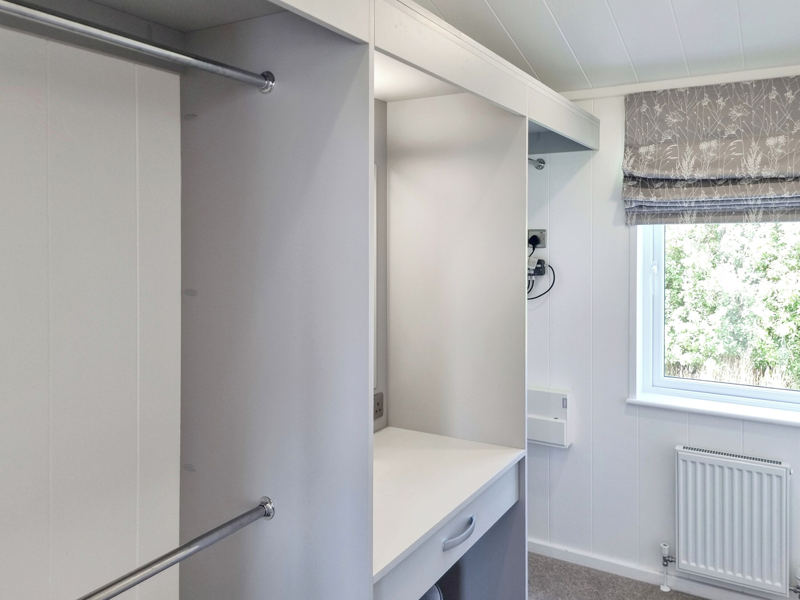 A walk-in closet with a built-in desk and shelving, a radiator, and a window with a view of greenery.