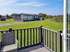 Une terrasse avec un fauteuil en osier, une pelouse verdoyante et une maison mobile en arrière-plan.