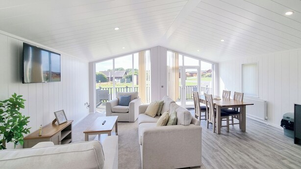 A spacious living area with a high ceiling, a flat-screen TV mounted on the wall, a sofa, a coffee table, and a dining table with chairs. - Cherry Blossom 43 - UK50711 (Fitling, near Burton Pidsea)