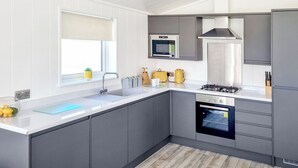 A modern kitchen with grey cabinets, a stainless steel range hood, a built-in oven, and a window with a view of the outdoors. - Cherry Blossom 43 - UK50711 (Fitling, near Burton Pidsea)