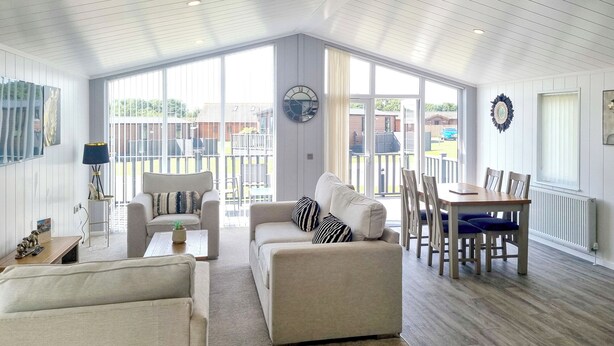 A spacious living room with a high ceiling, large windows, and a dining area with a table and chairs.