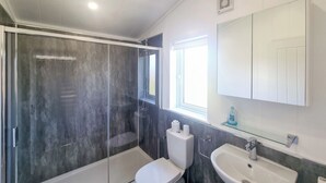 A modern bathroom with a glass-enclosed shower, a toilet, a sink, and a window providing natural light.