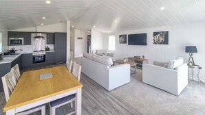 A modern kitchen with a dining area, a living room with a sofa and TV, and a hallway leading to bedrooms.