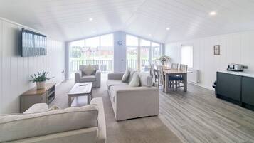 A spacious living area with a high ceiling, a dining table with chairs, a sofa, and a television mounted on the wall.