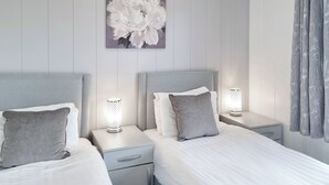 A modern bedroom with two beds, each with a headboard, bedside tables, and lamps.
