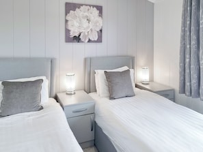 A modern bedroom with two beds, each with a headboard, bedside tables, and lamps.