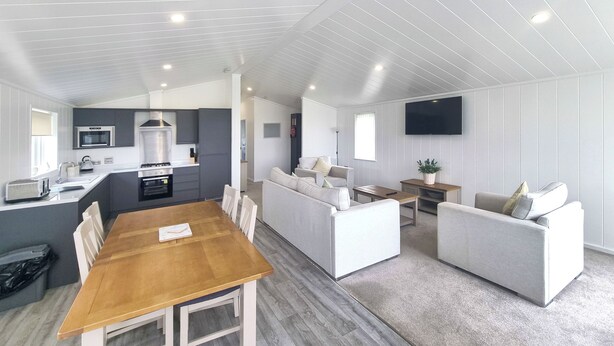 A modern kitchen with a dining area, a living room with a sofa, and a TV mounted on the wall.
